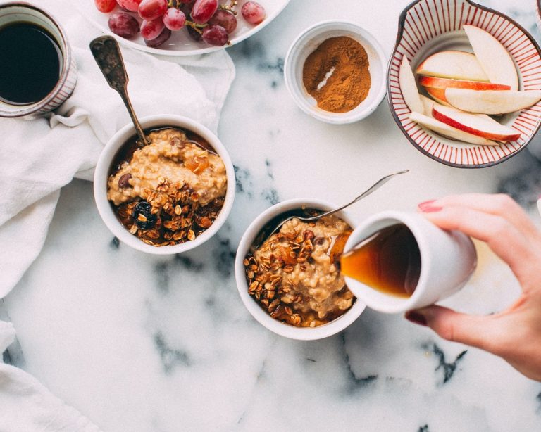 café da manhã ayurvédico: diferentes bowls com granola caseira, frutas, canela e uma mão segurando um potinho com mel e despejando o líquido em cima de um dos bowls com granola.