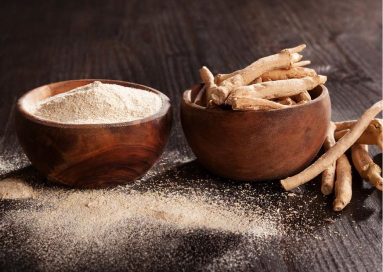 Dois bowls de cerâmica. à esquerda um bowl com farinha de raiz de Ginseng Indiano e no bowl da direita, a raiz in natura. Ambos estão sobre uma mesa de madeira com um pouco da farinha derramada.